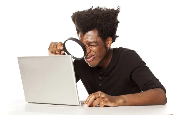 白い背景に彼のラップトップ コンピューターのトラフを虫眼鏡を見て若いアフリカ系アメリカ人の男 — ストック写真