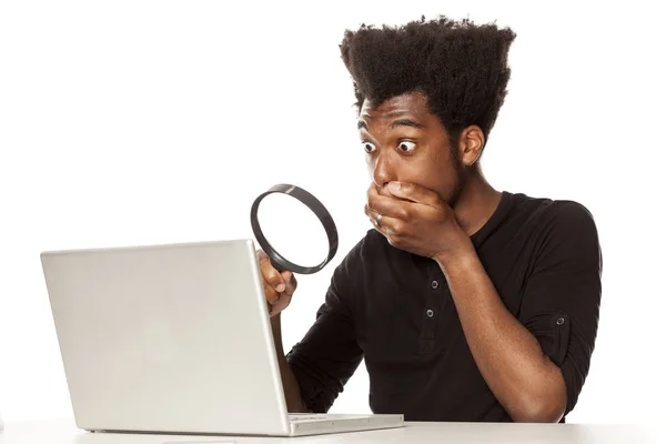 年轻震惊非裔美国人看着他的笔记本电脑在白色背景的放大镜 — 图库照片