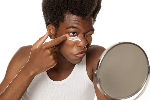 Joven Afroamericano Aplicando Crema Facial Bajo Sus Ojos Sobre Fondo —  Fotos de Stock