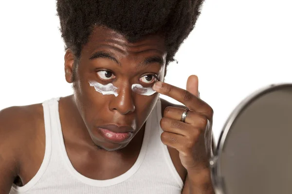 Joven Afroamericano Aplicando Crema Facial Bajo Sus Ojos Sobre Fondo — Foto de Stock