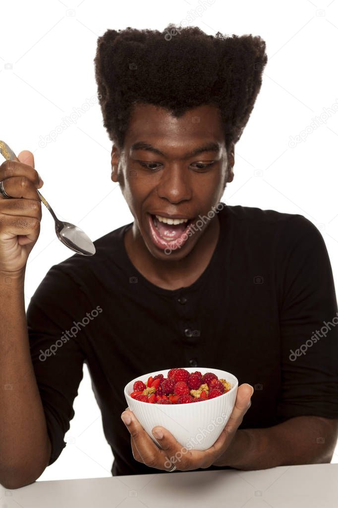 Young handsome Afro american hipster guy eating cereals with fresh fruits isolated on a white background. healthy food concept