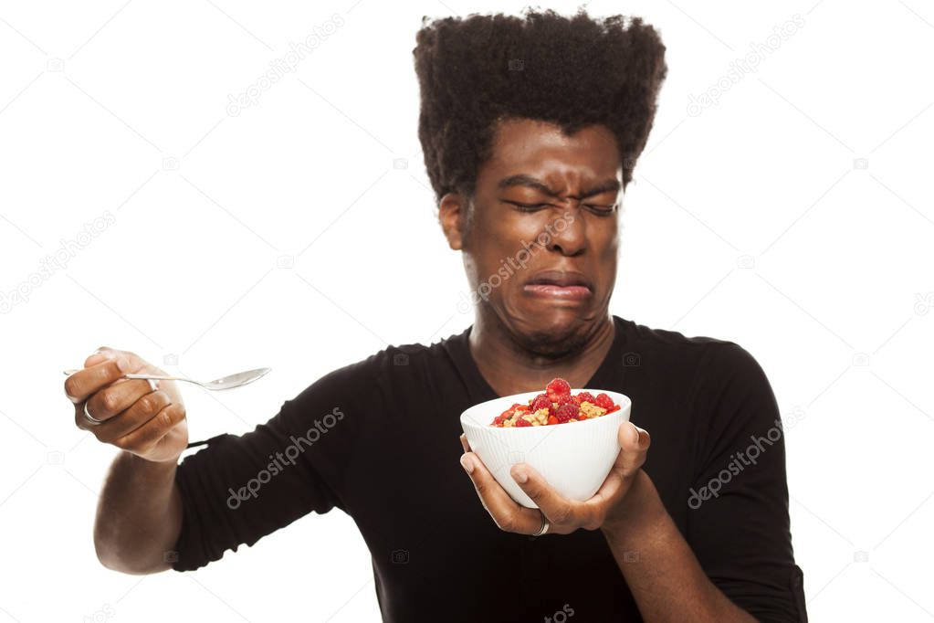 Disgusted young handsome Afro american hipster guy eating cereals with fresh fruits isolated on a white background. healthy food concept