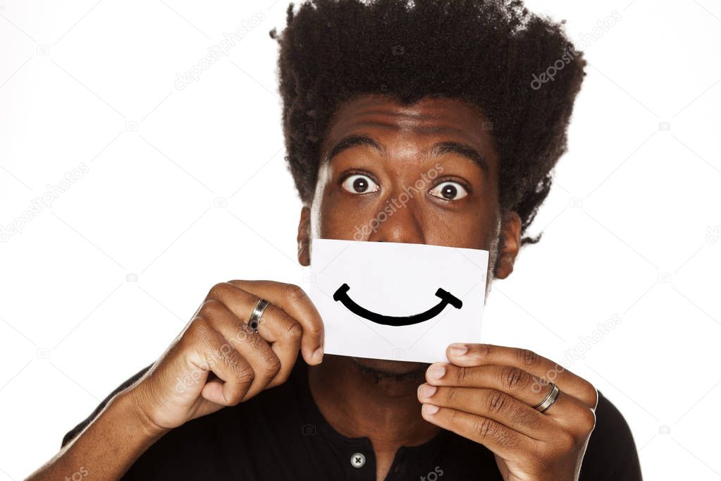 Happy young African man holding a smile drawn on a sheet of paper on a white background