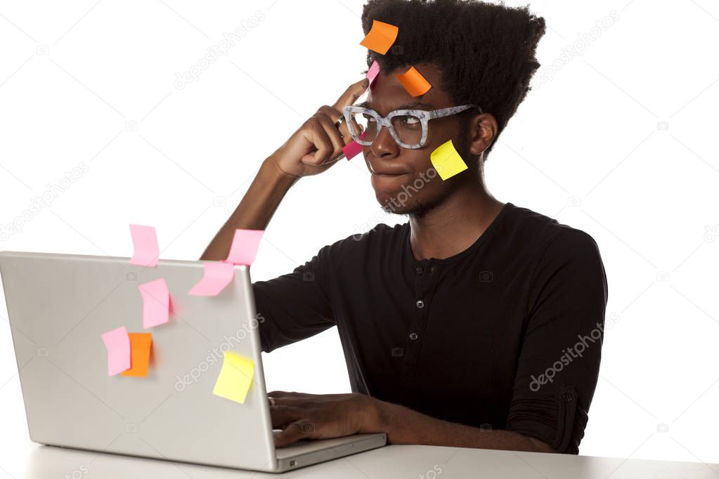 Confused young African man with stickers on his head sitting at a computer on a white background