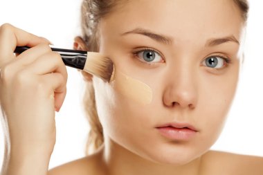 Genç kadının yüzünde bir fırça ile sıvı temel uygulama 