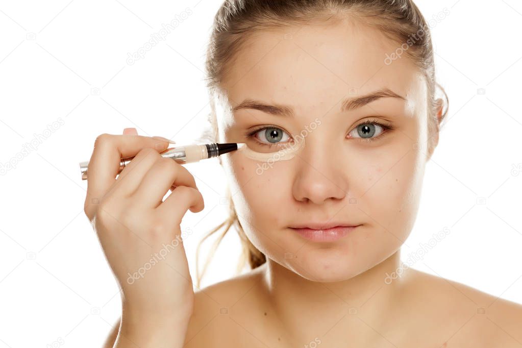 Young girl applying concealer on a white background