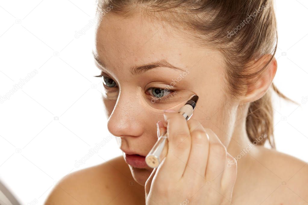 Young girl applying concealer on a white background