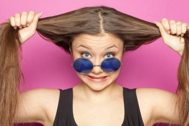 Mavi güneş gözlüğü ve ponytails üzerinde pembe bir arka plan ile genç kız