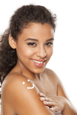 Beautiful dark skinned woman with body lotion on her shoulder on white background