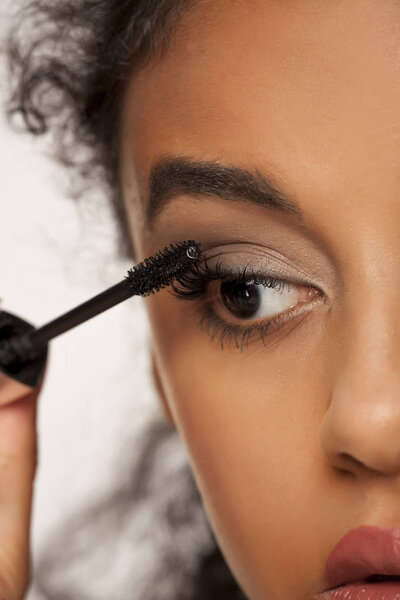 portrait of a young dark-skinned woman applying mascara on a white background