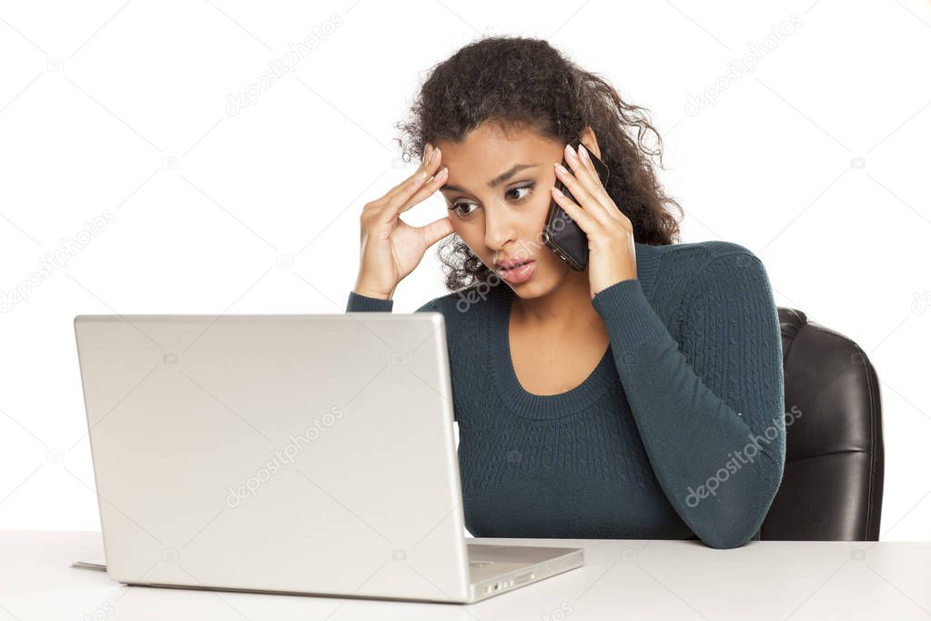 Beautiful dark skinned student talking on phone and working on her laptop on white background