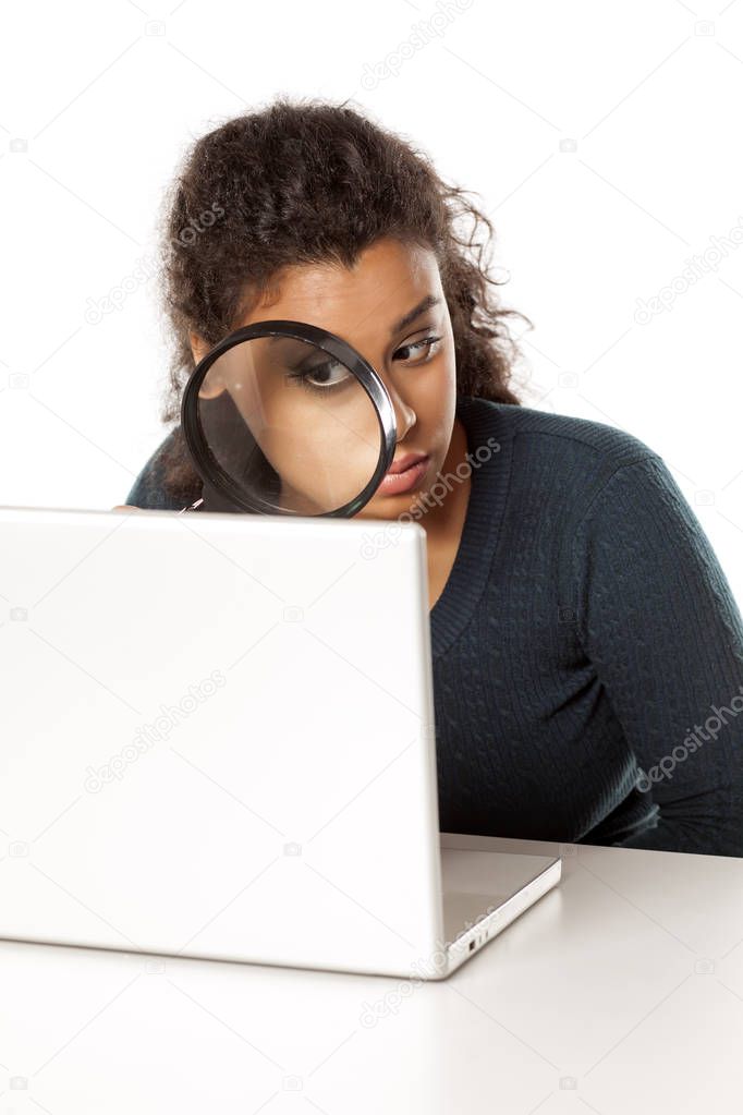 portrait of young dark-skinned woman with magnifying glass looking in her laptop on a white background