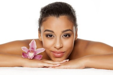 beyaz bir arka plan üzerinde yatan orkide ile genç güzel koyu tenli kadın portresi