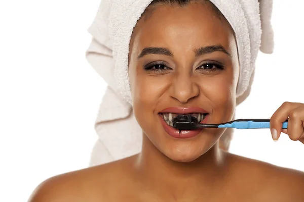 白い背景に黒い歯磨き粉で歯を磨く幸せな若い黒い肌の女性の肖像画 — ストック写真