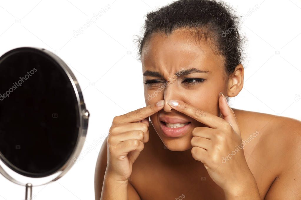 portrait of young dark-skinned woman squeeze a pimple on white background