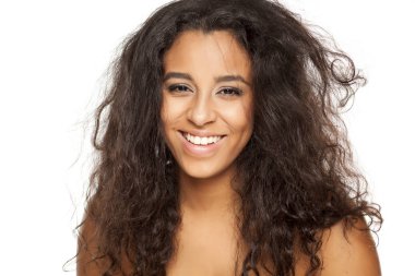 beyaz bir arka plan üzerinde dağınık uzun saçlı gülümseyen genç koyu tenli bir kadının portresi