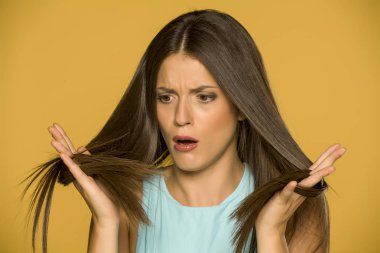 Shocked young woman looking at her hair on yellow background