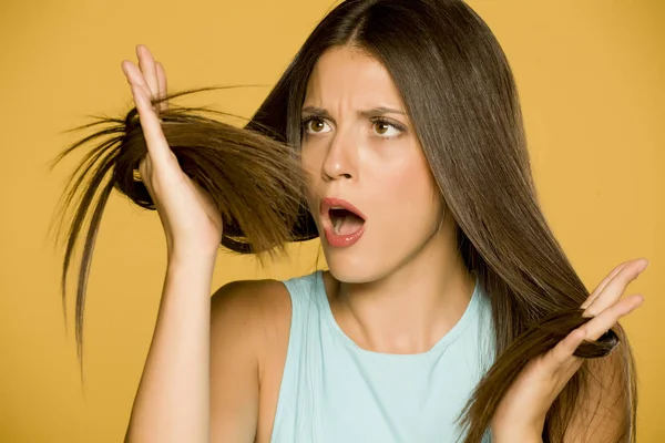 Шокированная Молодая Женщина Смотрит Свои Волосы Желтом Фоне — стоковое фото