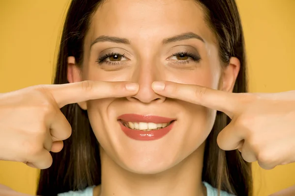 Güzel Genç Mutlu Kadın Sarı Arka Plan Üzerinde Parmaklarıyla Burnuna — Stok fotoğraf
