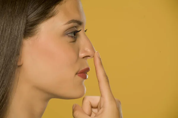 Güzel Genç Kadın Sarı Arka Plan Üzerinde Parmağıyla Burnuna Dokunarak — Stok fotoğraf