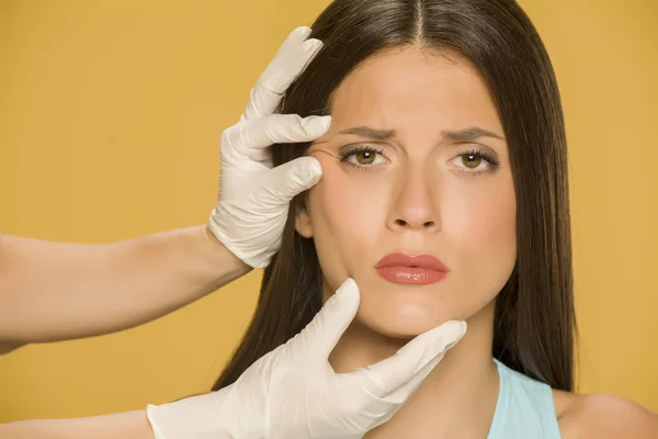 Ręce Lekarza Kontroli Wrincles Młodej Kobiety Żółtym Tle — Zdjęcie stockowe