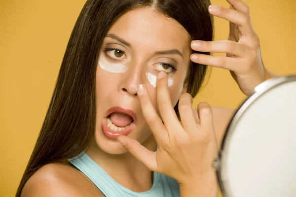 Young Woman Applying Creme Her Low Eyelids Yellow Background — Stock Photo, Image