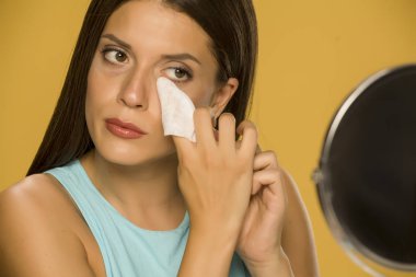 Genç kadın sarı arka planda ıslak mendil ile yüzünü temizliyor