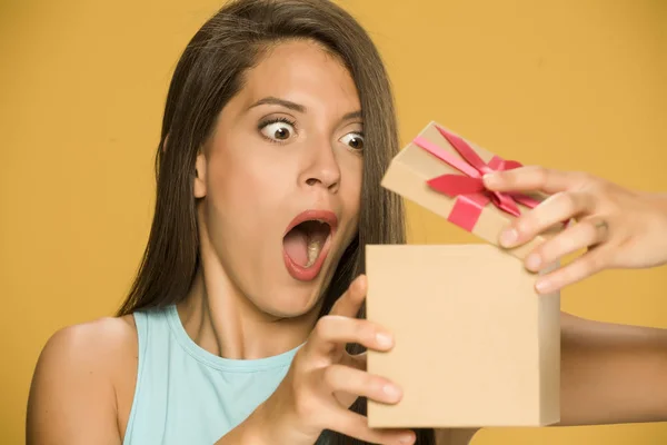 Young shocked woman opening a present box on yellow background