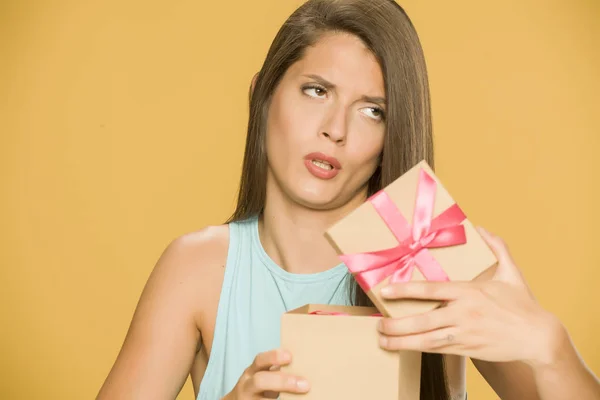 Young disappointed woman opening a present box on yellow background