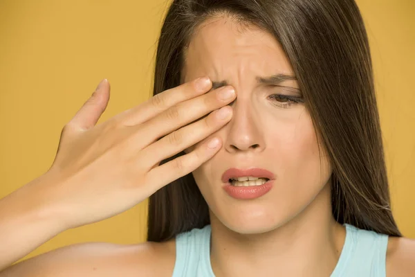 Young woman with pain in the eyes on yellow background