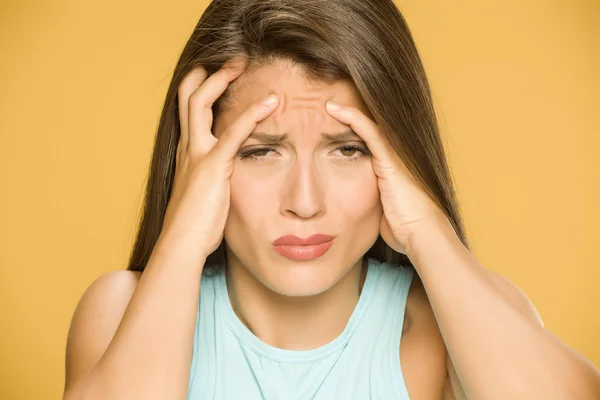 Young woman with strong headache on yellow background