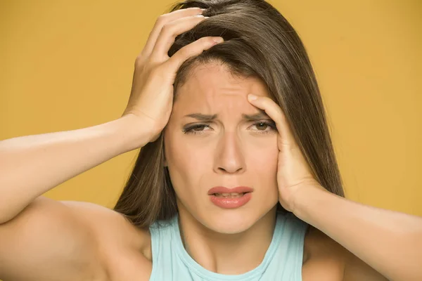 Young woman with strong headache on yellow background