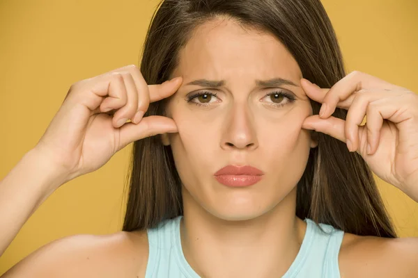 Junge Besorgte Frau Kneift Ihre Augenfalten Auf Gelbem Hintergrund — Stockfoto