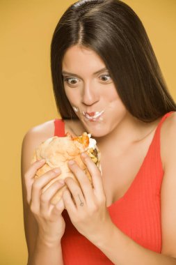 Genç açgözlü kadın sarı arka planda bir burger yemek