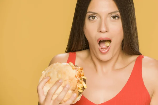 Young happy woman eating a burger on yellow background