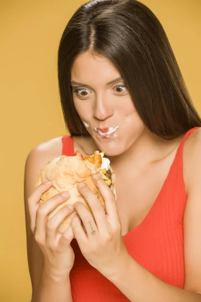 Young greedy woman eating a burger on yellow background