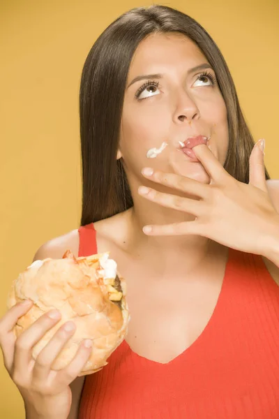 Young greedy woman eating a burger on yellow background