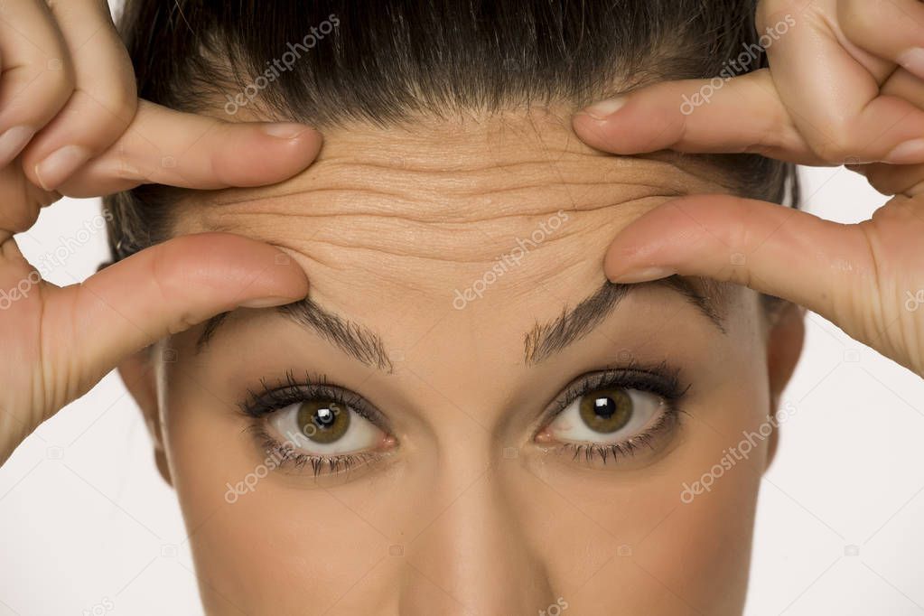 young woman pinching her forehead wrinkles with her fingers on a white background
