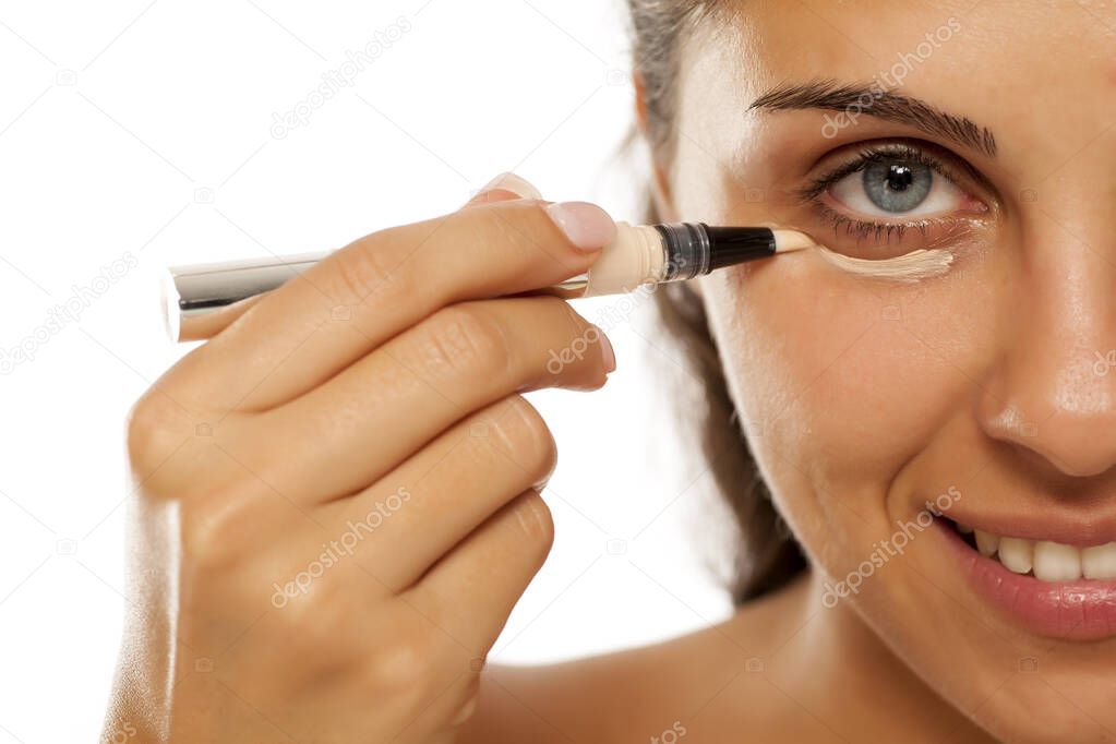 A young woman applies a concealer under the eyes