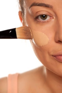 Beyaz arka planda fırçayla sıvı temel uygulayan genç bir kadın.