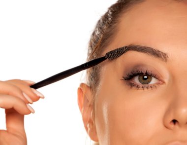 Beyaz arka planda kuru fırçayla kaşlarını şekillendiren genç bir kadın.