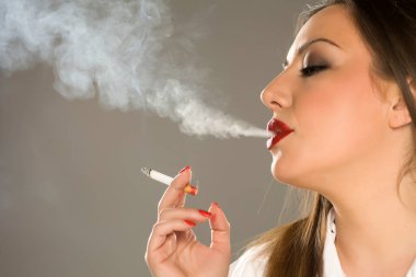 Gri arka planda sigara içen makyajlı ve uzun saçlı güzel bir kadının portresi.