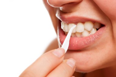 Genç bir kadın dişlerini plastik bir kürdanla temizliyor.