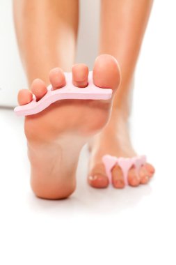 Beyaz arka planda tırnak cilası ayırıcısı olan bir kadın ayağı.