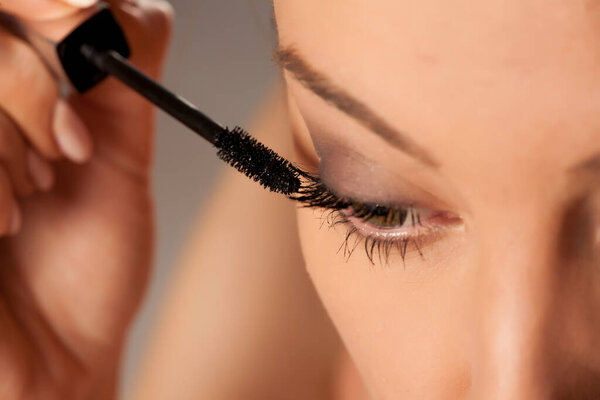 Young woman applying mascara on white background