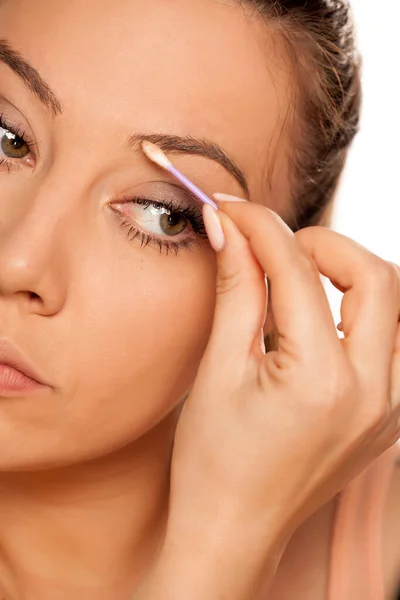 Young woman contouring her eyebrows with cotton swab on white background