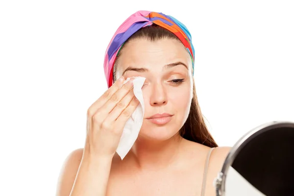 一个年轻漂亮的女人在白色的背景上用湿巾擦拭她的脸 — 图库照片