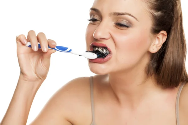 年轻女子在白底上用活性炭的黑色牙膏刷牙 — 图库照片