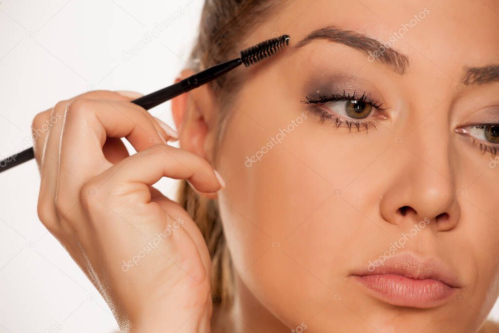 Young woman contouring her eyebrows with dry brush on white background
