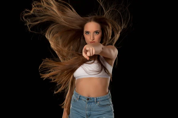 Young woman with very long flying hair on black background pointing on you